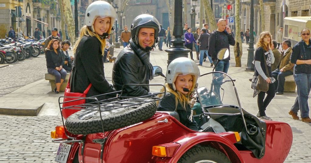 Red sidecar motorcycle with private tour guide and two young female tourists in Barcelona's El Born neighborhood.