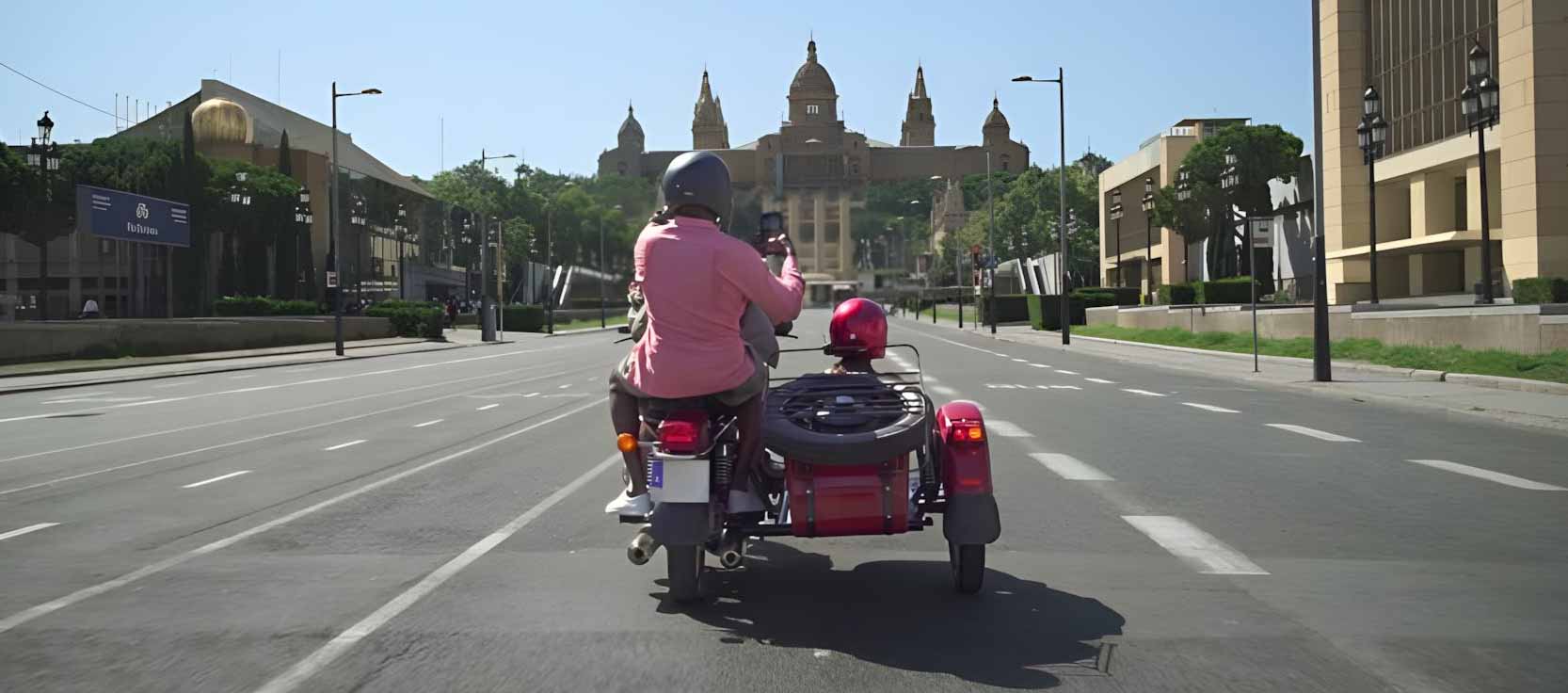 Tour guide and a tourist couple on a red sidecar motorcyle arriving at Palau Nacional during a tour of Barcelona.